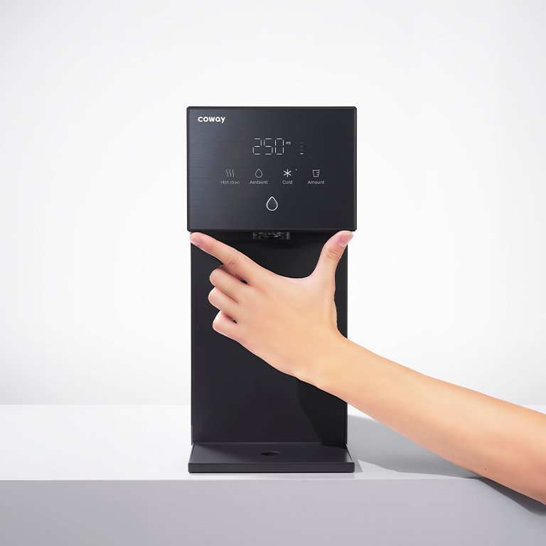 A hand reaching to the Coway Dazzie touch panel on a bright countertop