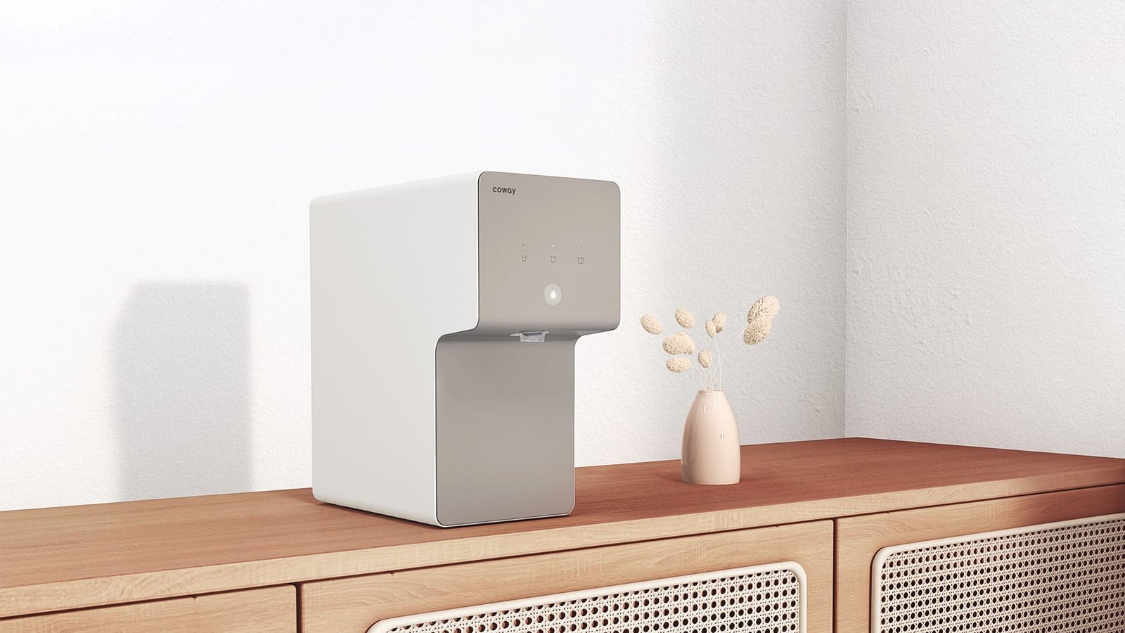 Coway Cinnamon water purifier on a wooden cabinet beside a vase of dried flowers